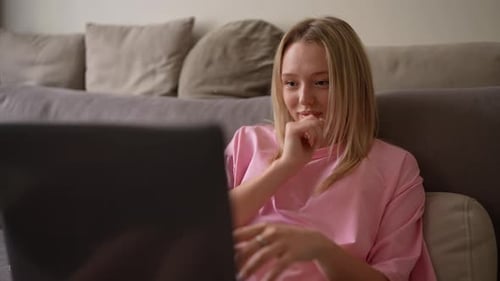 Close Up of Happy Blonde Girl in Pink Tshirt Smiling and Typing on Her Gray Laptop at Home