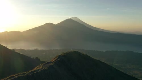 Female adventure hiker standing on ridge cheering in winning gesture with view of volcano, Bali