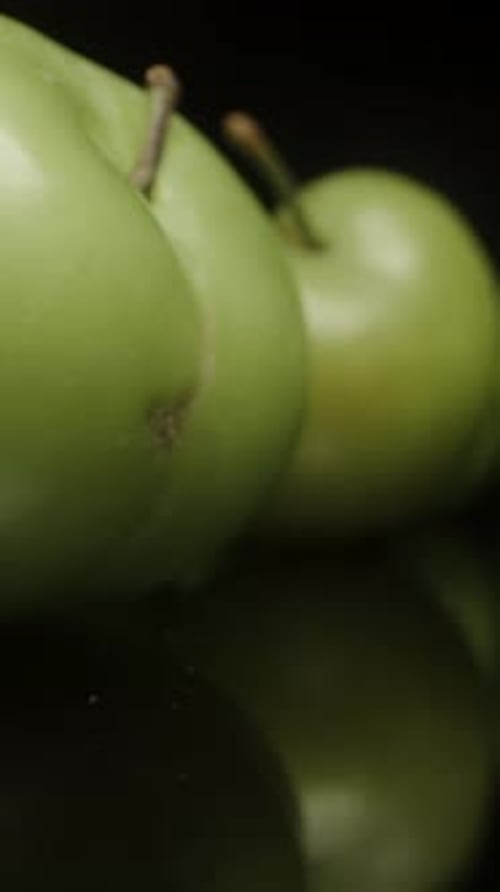 Vertical video. Scattered Unripe Green Cherry Plum Fruits on Black Mirrored Table. Dolly Slider