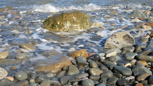 Sunny blue ocean tide washing over colourful stone pebble beach holiday scene dolly right