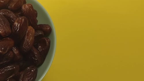 Bowl of Brown Dates on Yellow Background