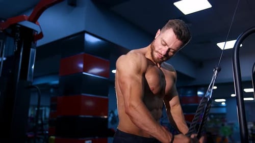 Fitness man pumping up arm muscles. Bodybuilder doing arms exercises with naked torso in gym.