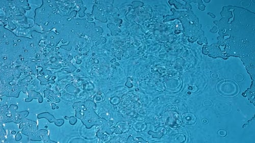 De belles gouttes d'eau de surface semi-séchées de couleur bleue tombant du haut créent un effet de pluie lent