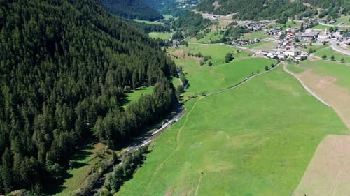 Green valley between huge mountain ranges with fields and a small village under a blue sky, drone pa