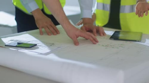 Team of Engineers are Bending over Large Blueprint and Having Conversation, inside Building Under C