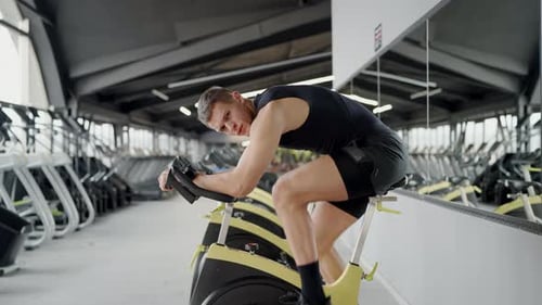 Muscular Man Exercising on Stationary Bike in Gym