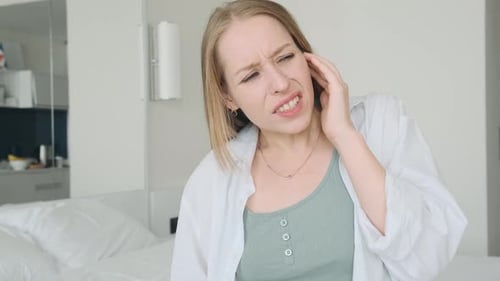 Young Woman Suffering From Strong Ear Pain Upset Female with Tinnitus and Otitis Sitting at Home and
