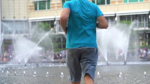 Sporty man finishes jogging and rests by city fountain in super slow motion