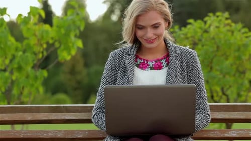 Woman Working on Laptop Outdoors on Park Bench
