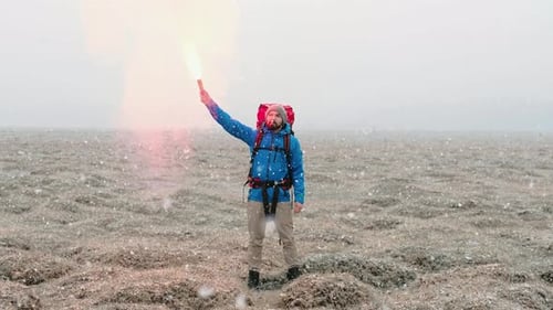 Lone Hiker Signals with Flare in Snowy Landscape