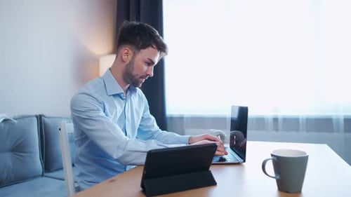 Young Man Sits at Home on the Desk and Works Using a Laptop Financial Manager on a Remote Work Slow