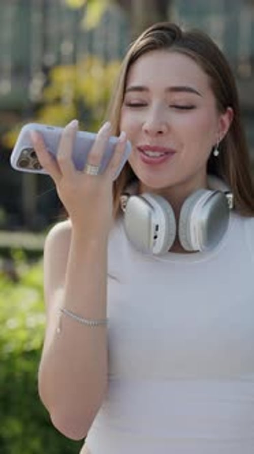 Portrait of Happy Woman Records Voice Message on Smartphone in Public Garden