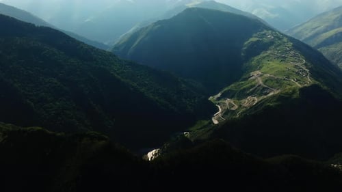 Aerial Shot of a Secluded Village Along a River in a Deep Mountain Valley with Serpentine Roads