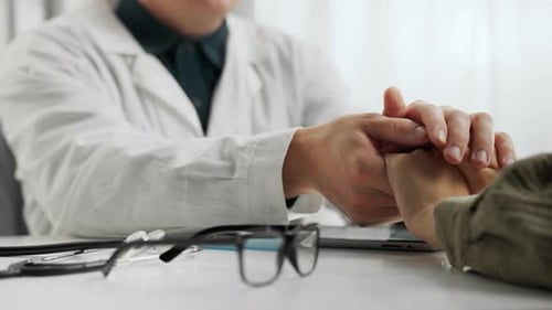 Doctor Comforting Patient by Holding Hands in Clinic