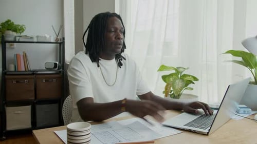 Black Entrepreneur Using Laptop and Documents at Desk in Home Office
