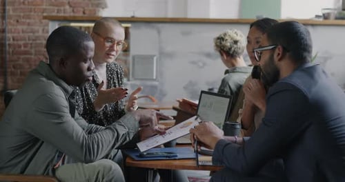 Diverse Business Team Men and Women Talking Using Laptop Sitting at Desk in Coworking Office