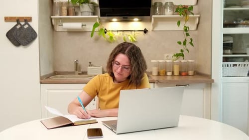 Woman Works on Laptop, Writes in Notebook at Home