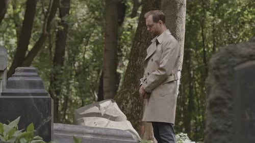 Grieving Man Standing by Gravestone at Cemetery