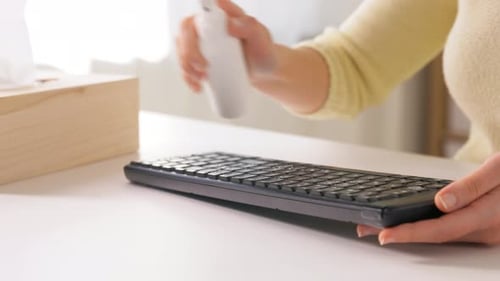 Woman Cleaning Keyboard with Sanitizer and Paper Towel