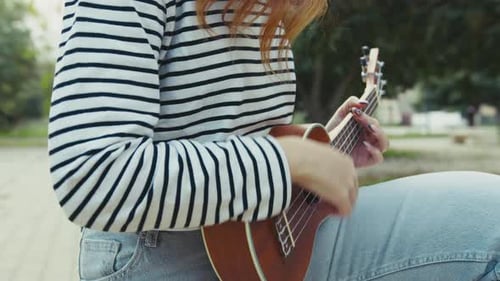 Artist Young Women Plays Ukulele Musical Instrument Outside In Park