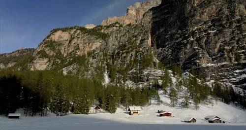 Snowy mountain landscape with winter vegetation. Wooden houses and cabins. Tilt down shot