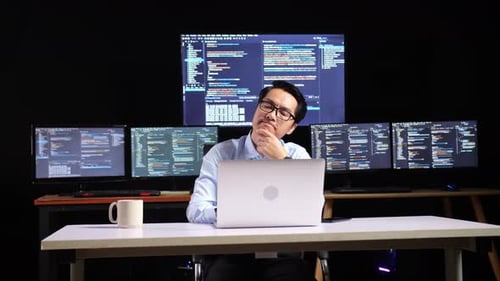 Programmer Thinking About Something While Writing Code By A Laptop Using Multiple Monitors