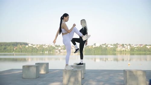 Fitness Together Two Women Do Fitness on the Shore of the Lake on Large Stones in a Warm Sunny Day