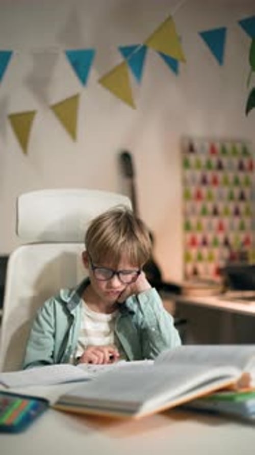 A Kid Wearing Glasses Sits on Table and Looks Bored He Doing Homework