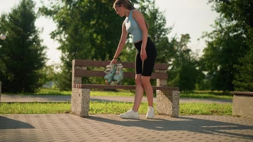 Young Lady Placing Roller Skates on Bench in Outdoor Park Setting