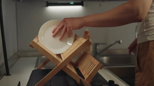 Person Placing Dishes in Wooden Drying Rack