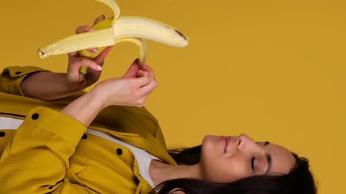 Woman Eats a Banana Lying on a Yellow Background
