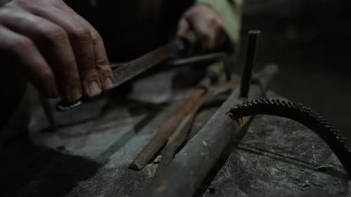 Artisan Hands Sharpening Iron Tools with File, Traditional Blacksmith Craftsmanship in Rustic Worksh