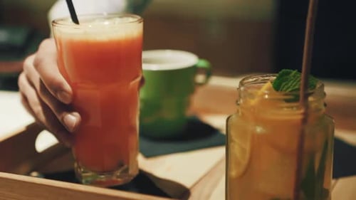 Placer à la main un grand verre de jus d'orange frais avec une paille à côté d'un pot de limonade à la menthe et