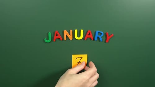 Hand sticking a sticker 7 January calendar day on school board. 7 date of January. Seventh day