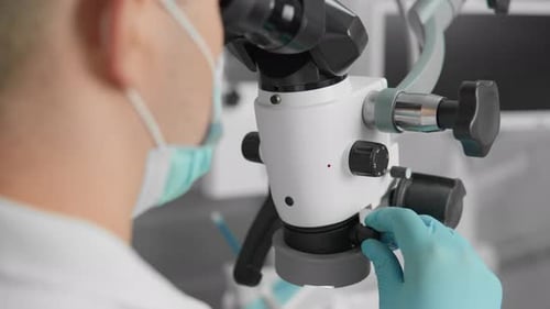 Dentist Surgeon Performs Surgery on a Patient's Tooth Under a Microscope in a Dental Clinic Closeup