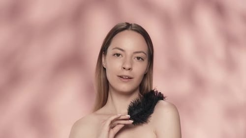 A Woman Touches Her Bare Shoulders with a Black Feather A Young Woman Demonstrates Smooth and Soft