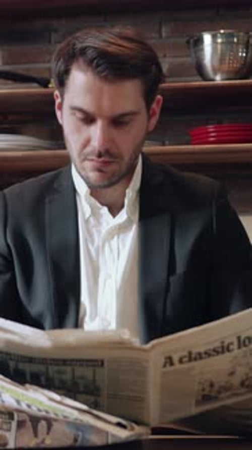 A Man is Engaged in Reading a Newspaper While Comfortably Seated in a Modern Kitchen Space