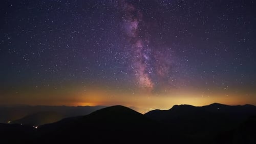 Time Lapse of the Milky Way the Silhouette of the Mountain Landscape the Night City Shining in the