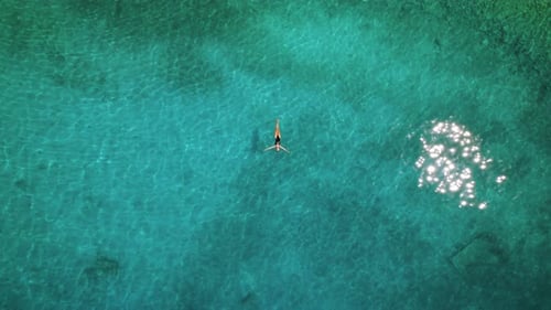 A lone swimmer floats in tranquil, clear waters, evoking a sense of peace. Serene Aquatic Solitude C