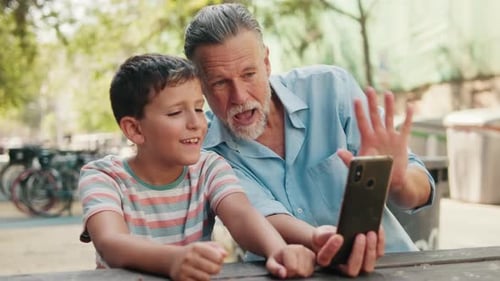 Grandfather And Grandson Video Chat At Park