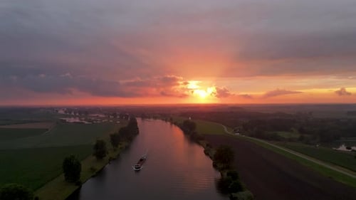 An aerial shot of a Beautiful sunset over Dutch river where a vessel passes by in an orange and red