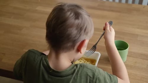 Young Boy Eating Noodles at a Wooden Table