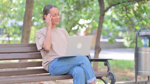 Woman Using Laptop on Bench in Urban Park