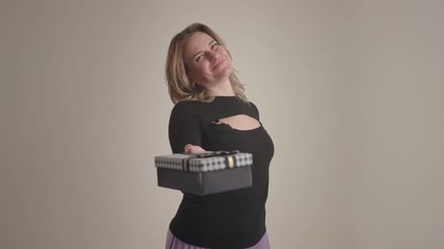 Femme présentant un cadeau en toute confiance posant joyeusement, idéale pour les célébrations et les campagnes de cadeaux