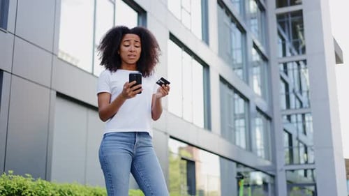 Woman Holding Phone and Card Looking Confused