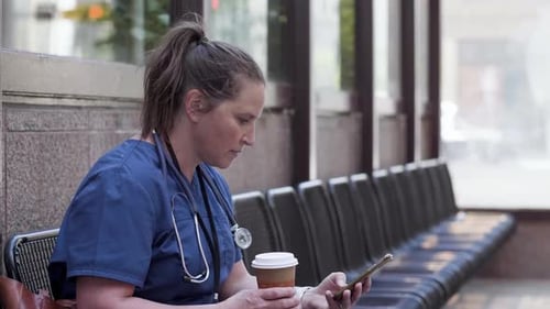 Nurse Texting on Phone in Covered Bus Stop Adult