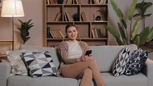 Woman Relaxing on Sofa with Smartphone at Home