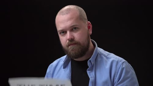 Close Up Footage Bald Bearded Man in a Blue Shirt on a Black Background Look in Camera and Shows the