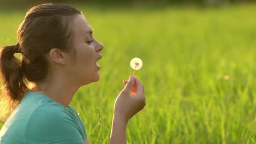 Woman Blowing Dandelion Seeds in Summer Field