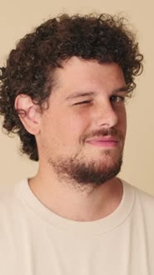 Close-up of man looking at the camera wink blink eye in studio on beige background